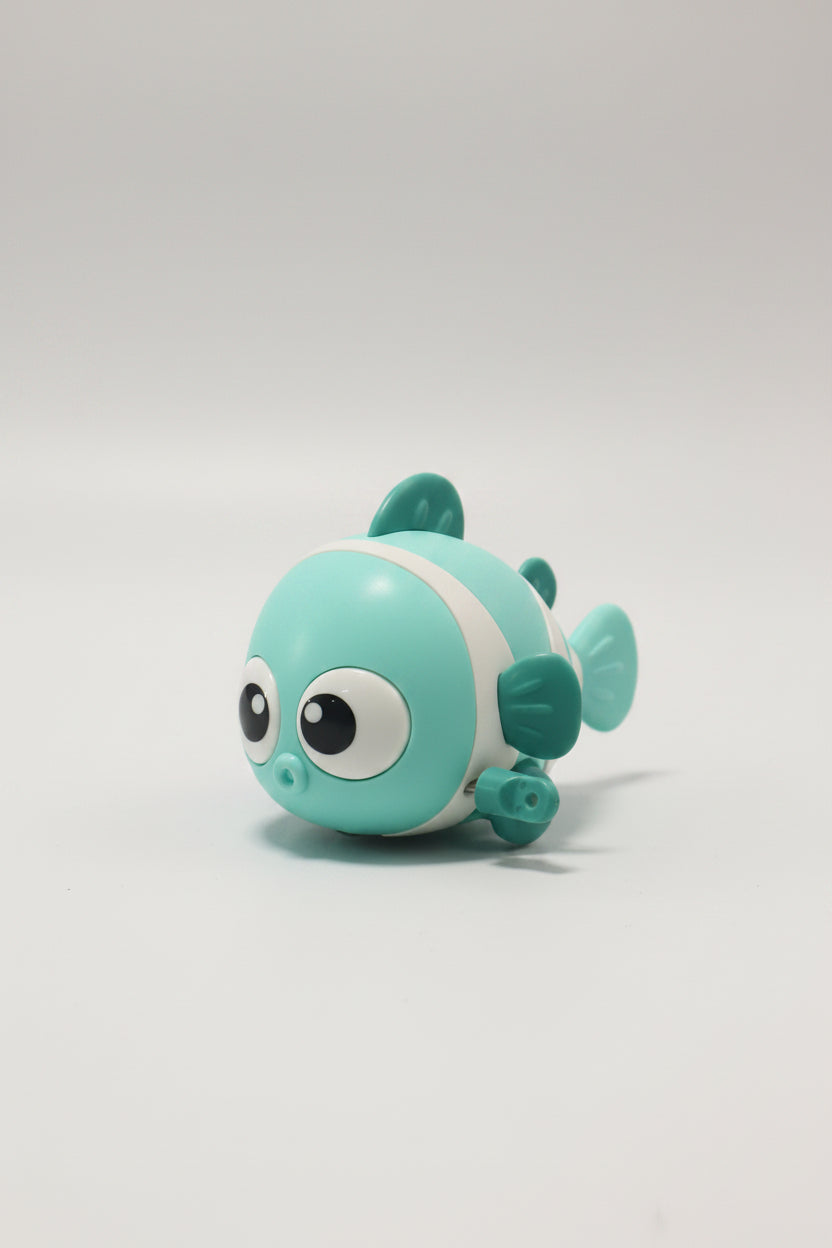 A small cartoon fish toy in mint green and white, resting on a reflective glass surface with a blurred store background.